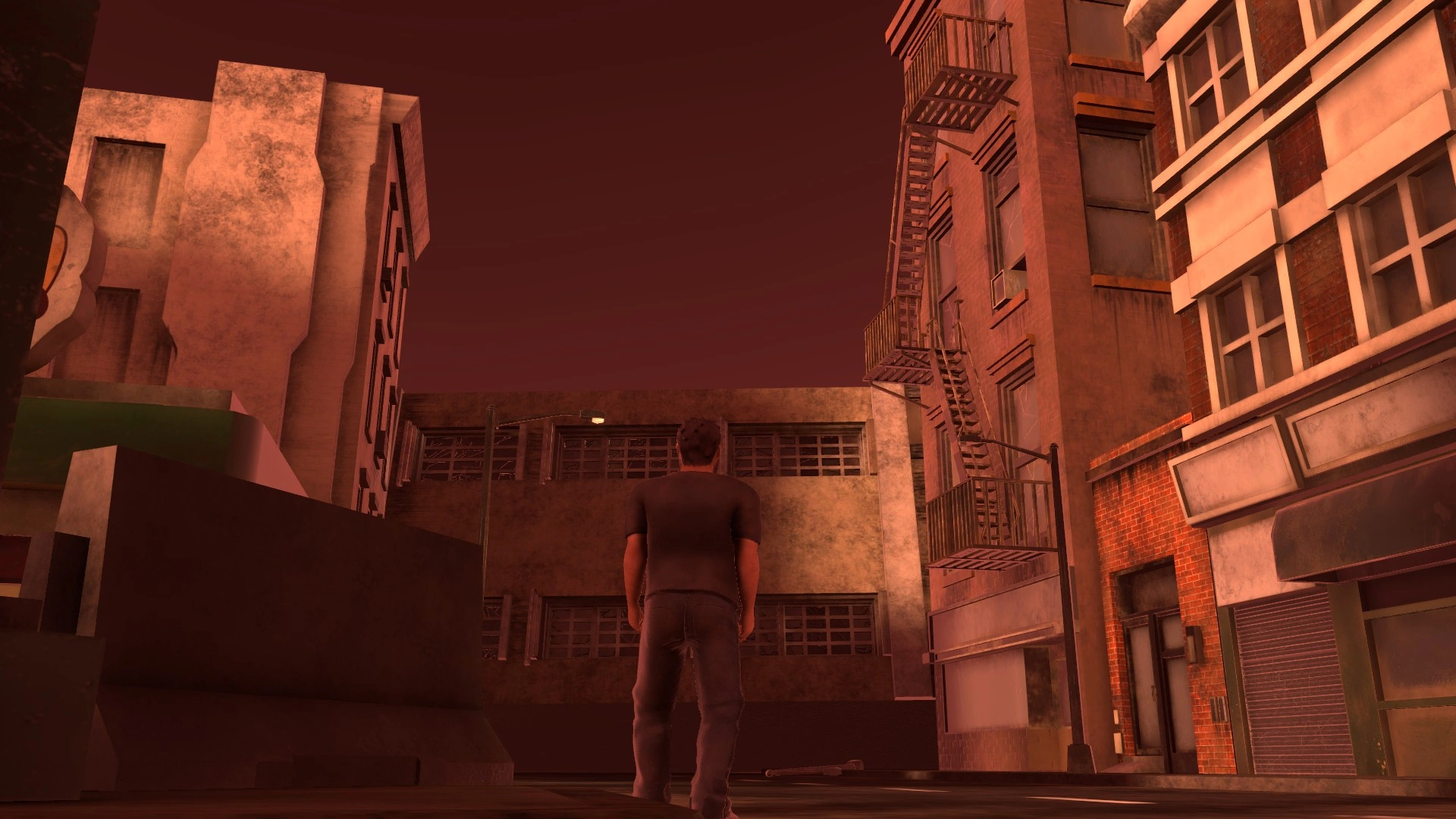 a 3d model of an adult male stands at the end of a post-apocalyptic city block. the exit is blocked by a fallen building. a fire escape can be seen next to the fallen building. the foreground is taken up by a concrete road block. the image is tinted red. the buildings and city block are covered in a coat of dust and grime